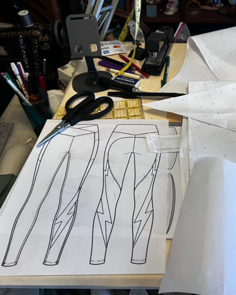 A desk with pattern paper, scissors, pencils, and the initial design for Sheer Fun leggings